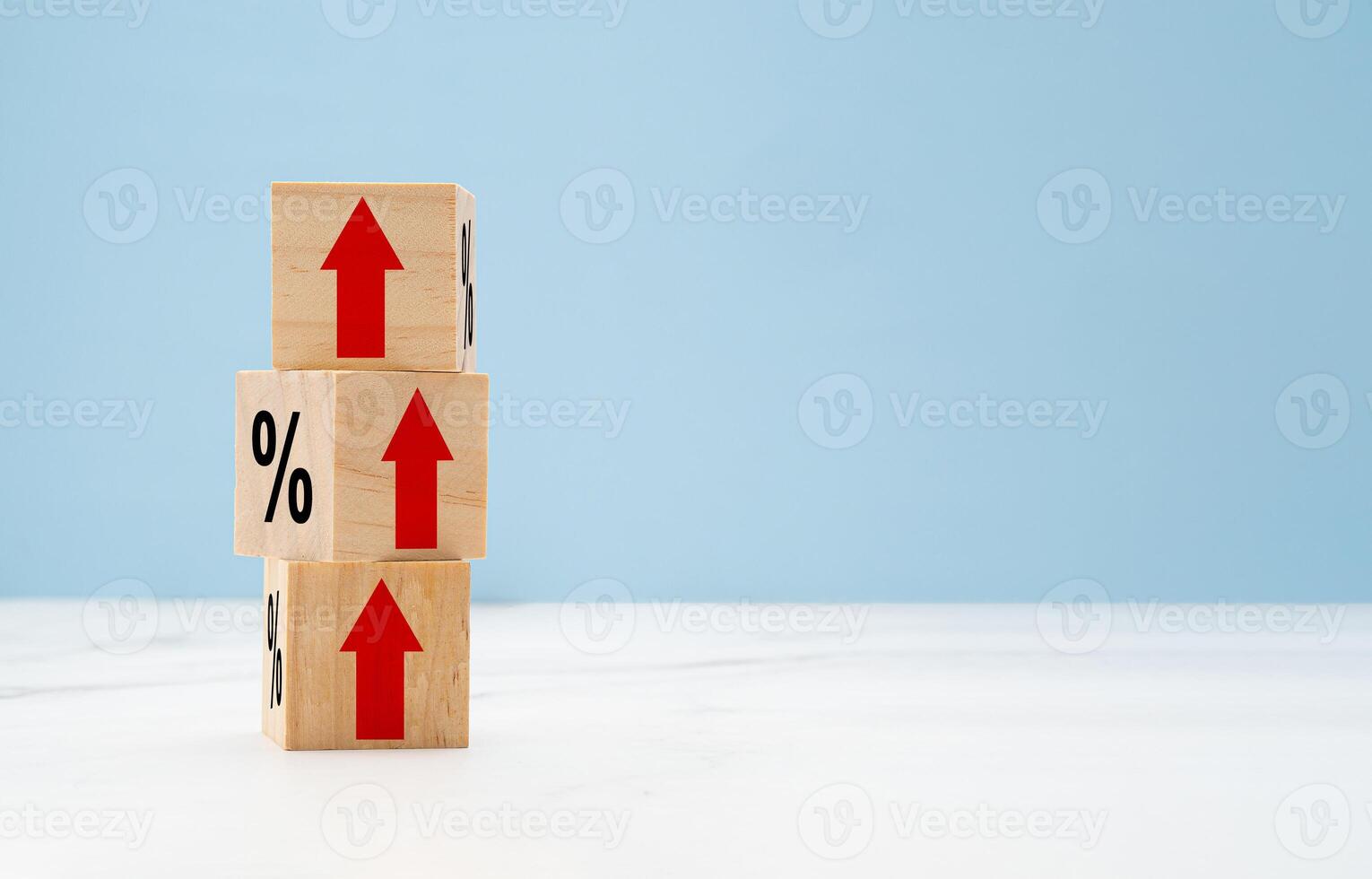 Wooden cubes with red arrows up and percent symbols on marble with a light blue background photo