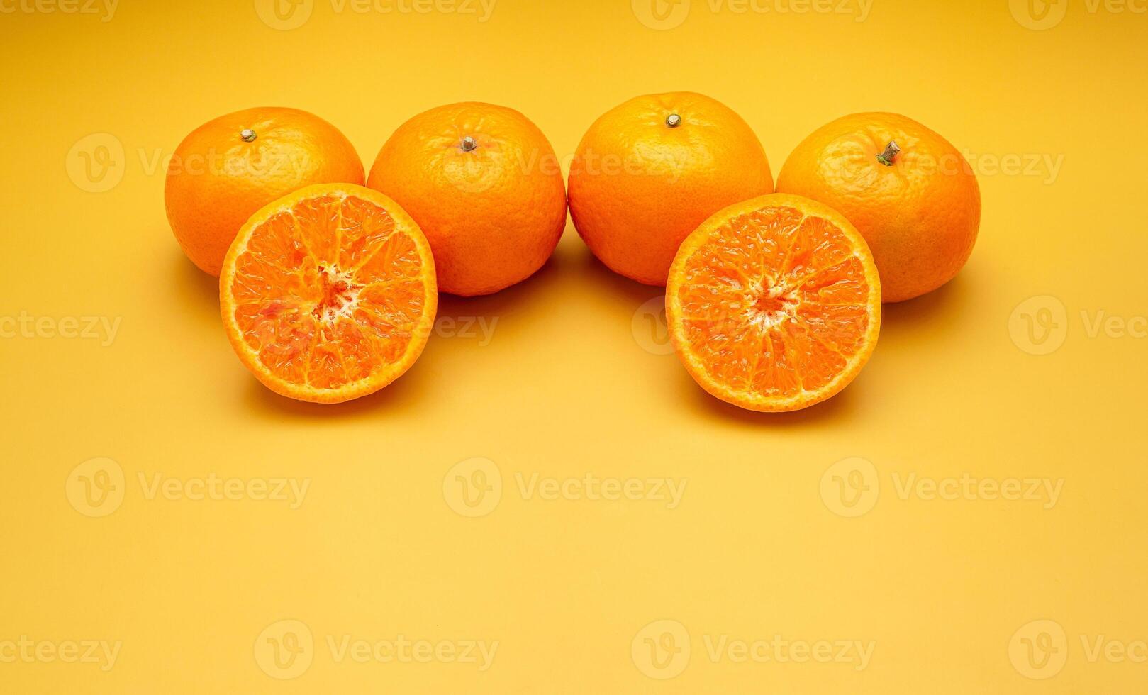 Pile of fresh oranges whole and half fruit on a yellow background with copy space for text photo
