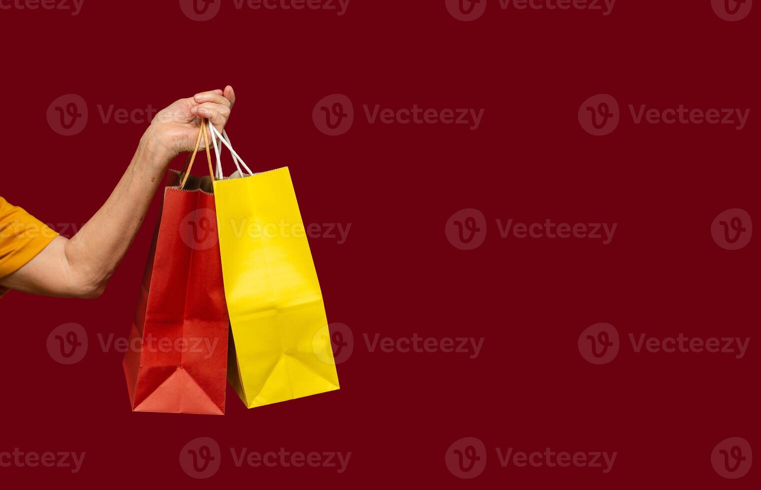 Close-up of hand holding yellow and red shopping bags with a handle while standing on a red background photo