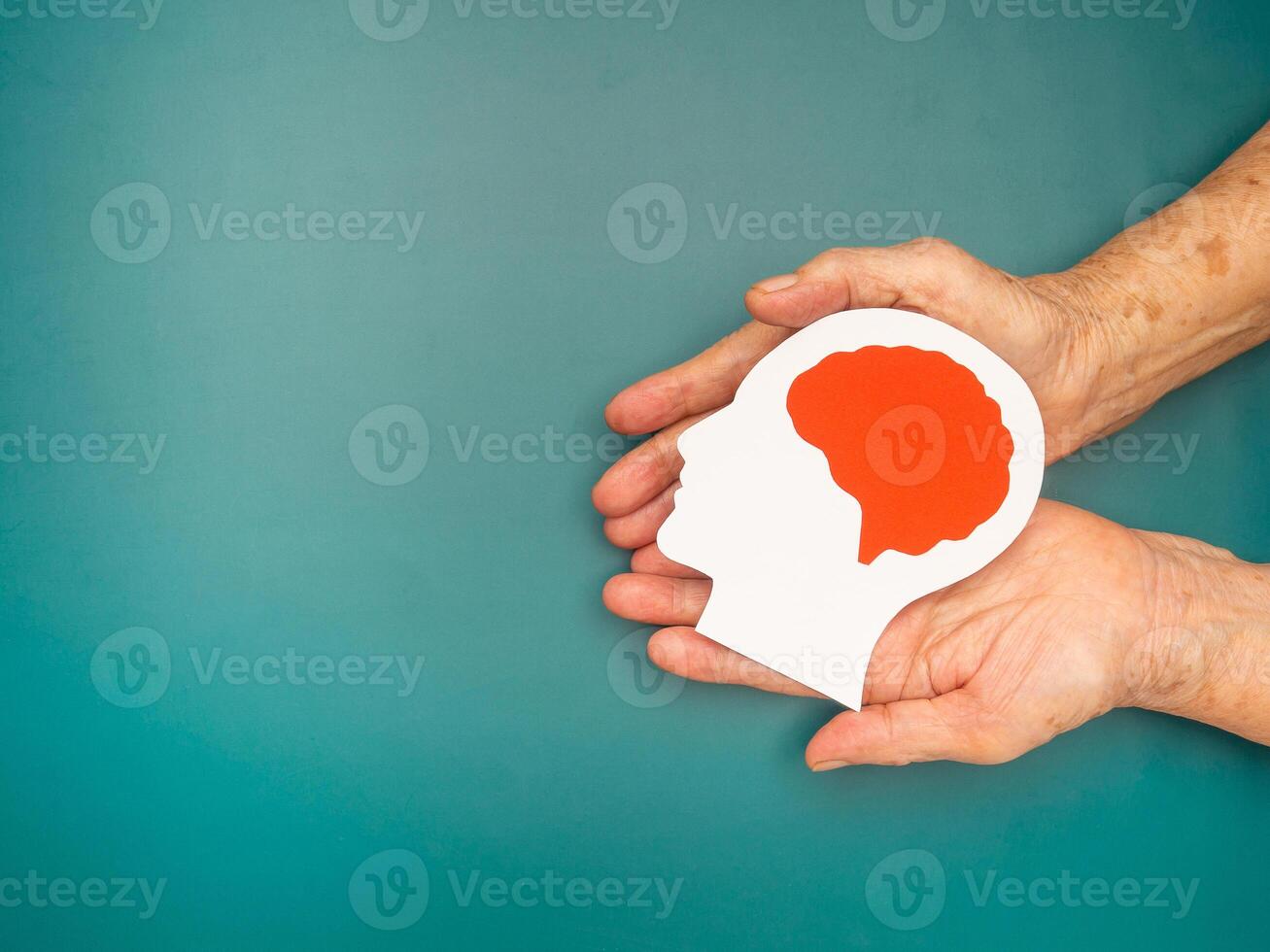Top view of head with a brain made from paper on the palm senior woman over a green background photo