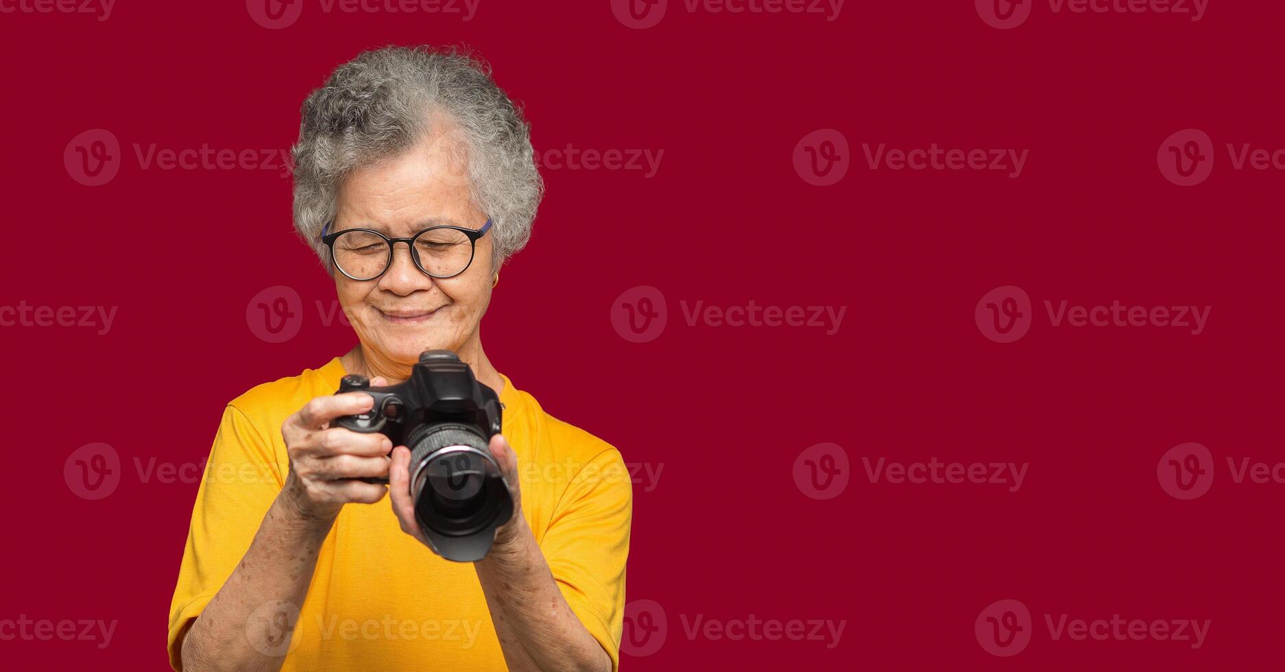 Happy senior woman looking at her photos in a digital camera while standing on a red background