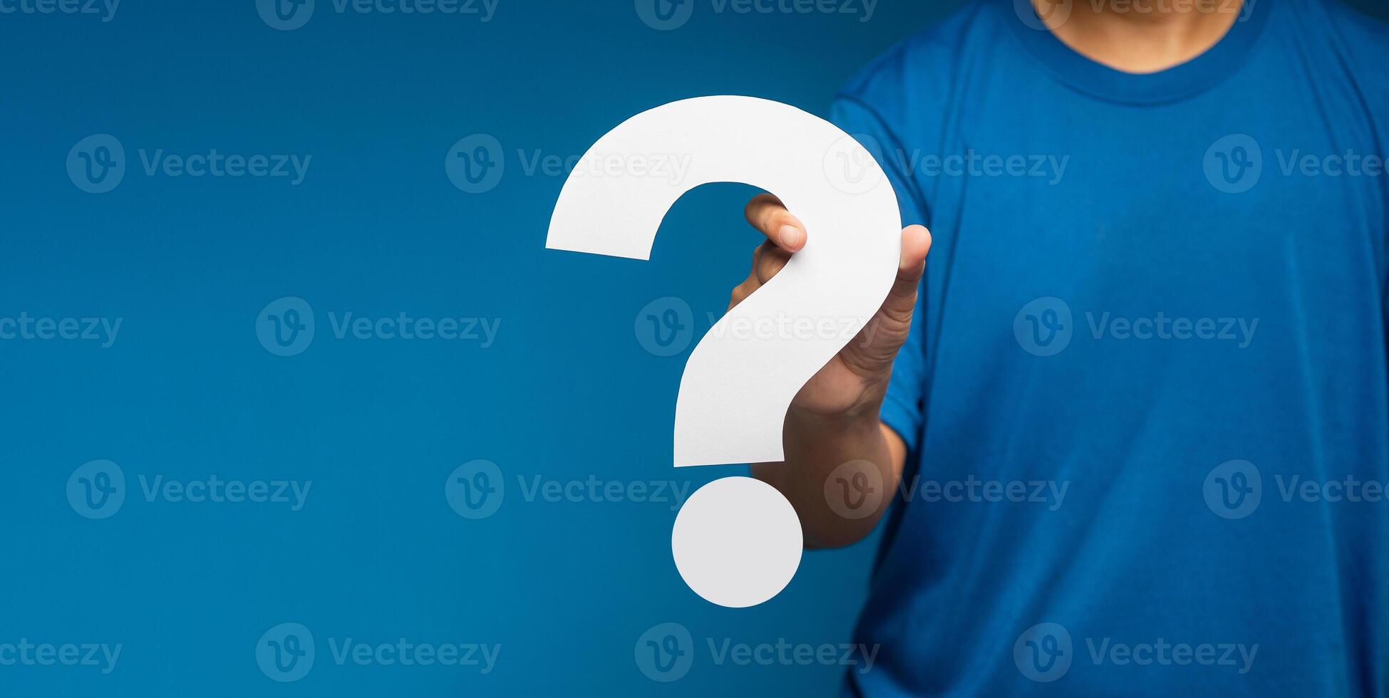 Businessman holding a white question mark paper while standing on a blue background photo