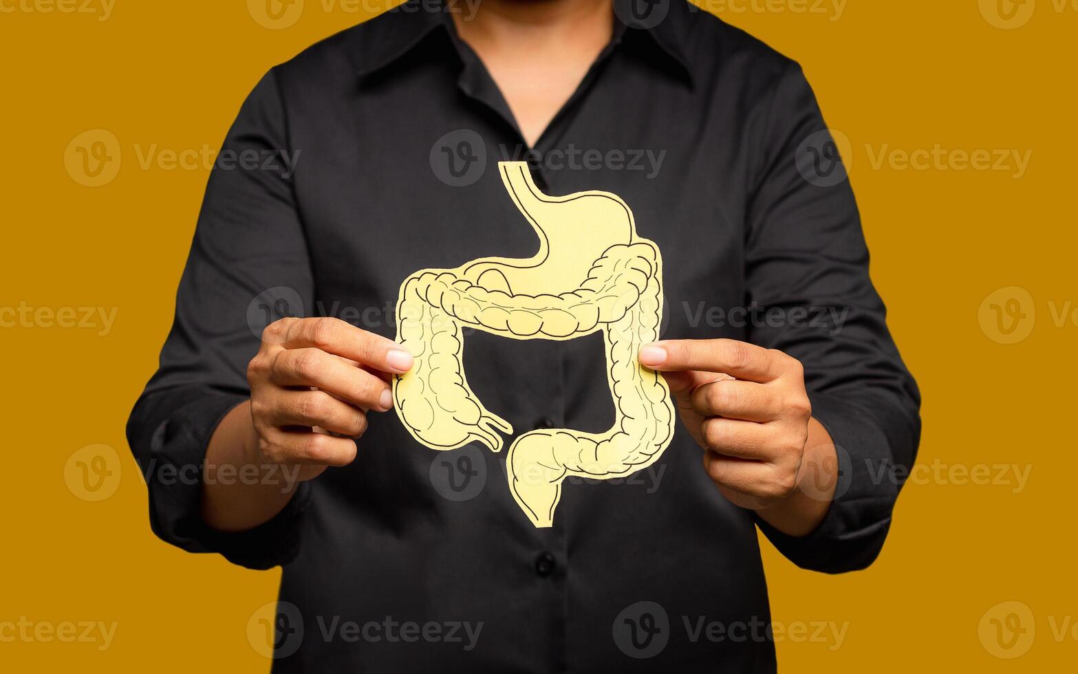 Close-up of hands holding a colon symbol while standing on a yellow background. photo