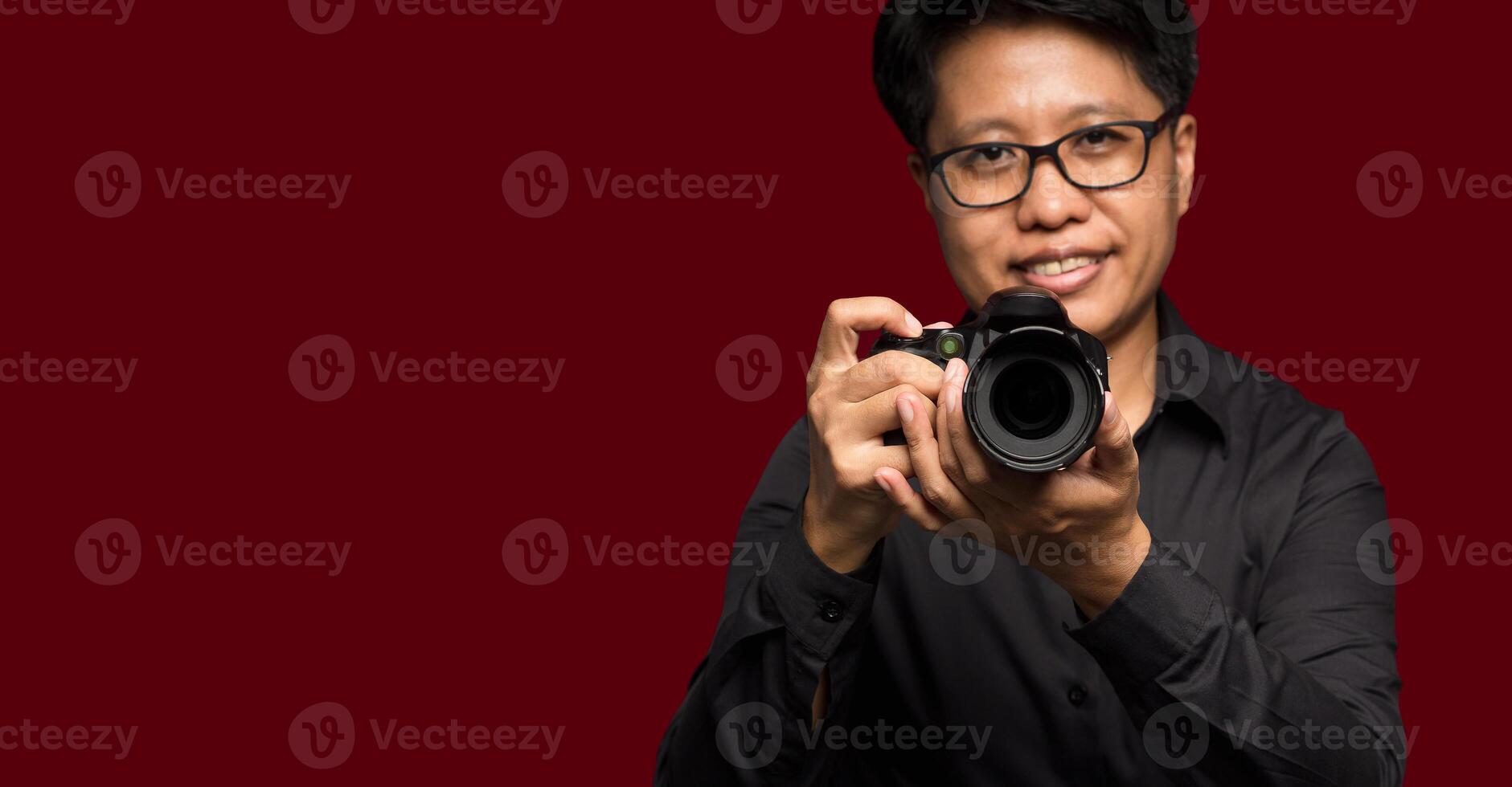 Portrait of a photographer in a black shirt holding a digital camera while standing on a red background photo
