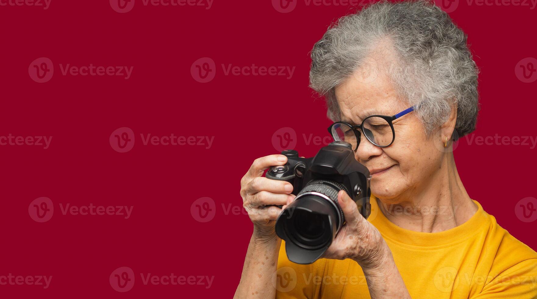 Senior woman taking photographs with a digital camera while standing on a red background photo