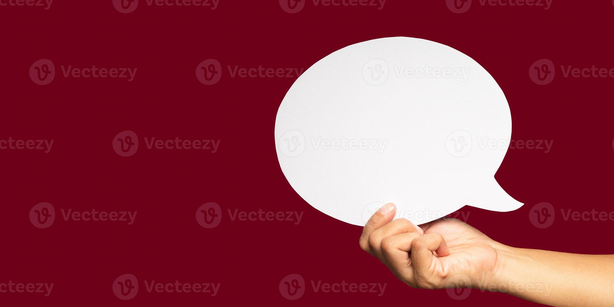 Close-up of hand holding a blank white speech bubble symbol over a red background photo