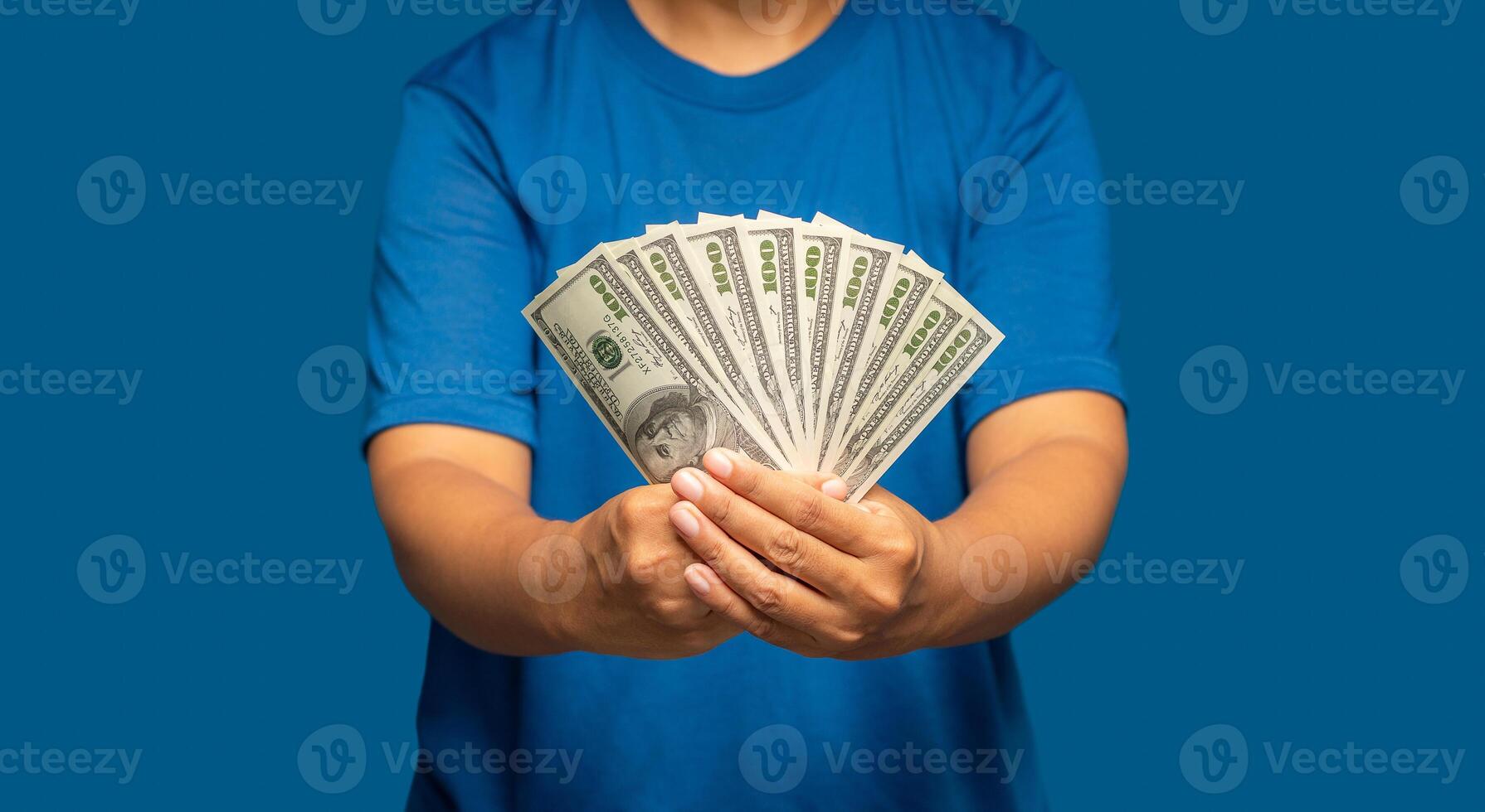 Man in a blue casual holding US banknotes while standing on a blue background. Business and finance concept photo