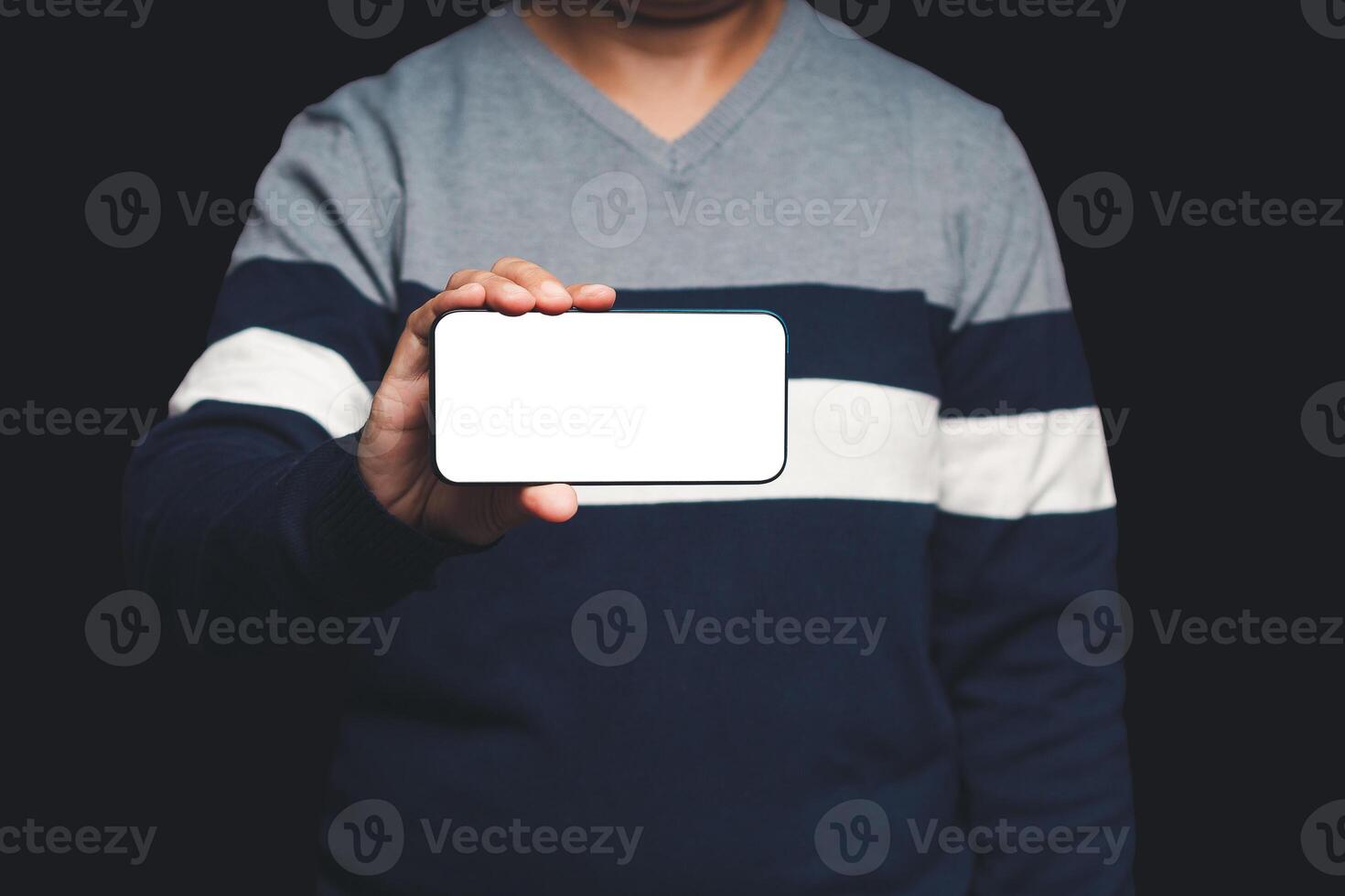Close-up of hand holding a horizontal mobile phone with a blank white screen while standing on a black background photo