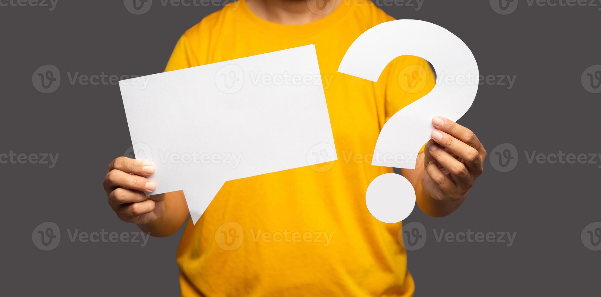 Close-up of hands young man holding a blank white speech bubble and a question mark symbol while standing on a gray background photo