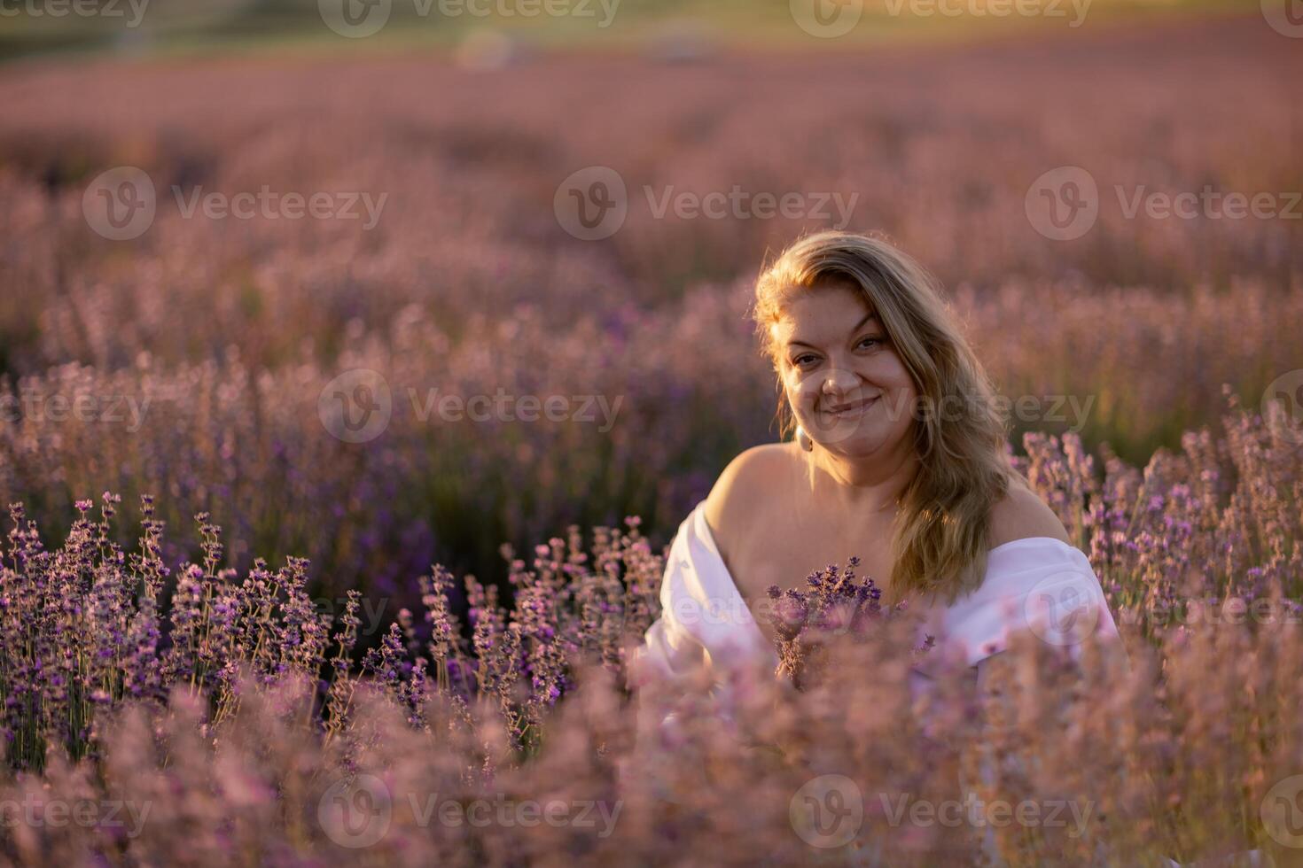 woman poses in lavender field at sunset. Happy woman in white dress holds lavender bouquet. Aromatherapy concept, lavender oil, photo session in lavender