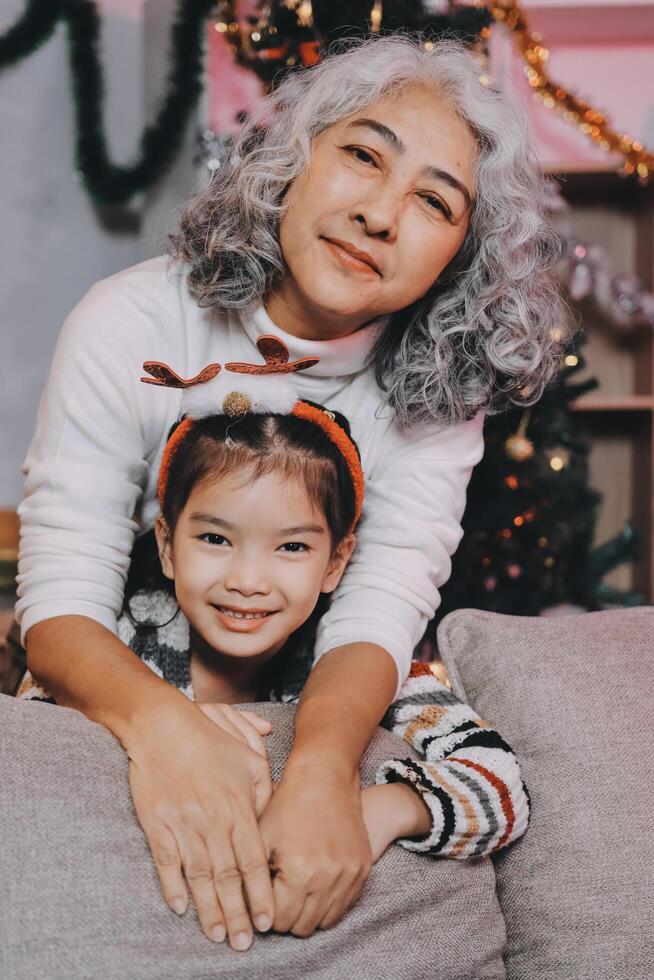 Happy family on Christmas morning. Affectionate grandmother and cheerful granddaughter open a holiday gift together at home photo