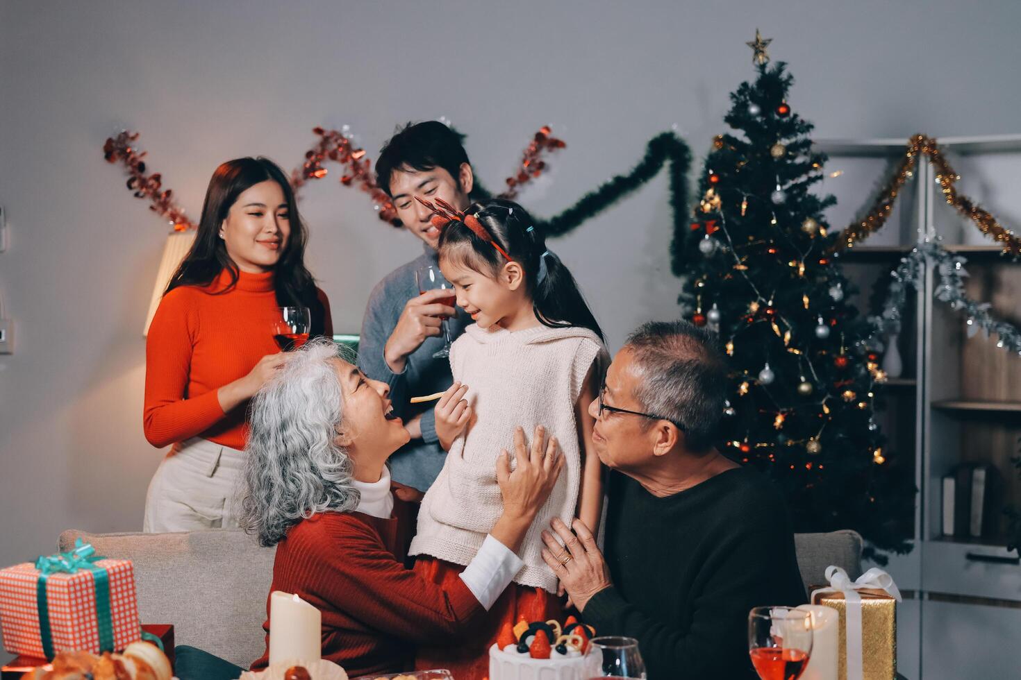 Multi-Generation Family Celebrate Christmas At Home Wearing Santa Hats And Antlers Opening Presents photo