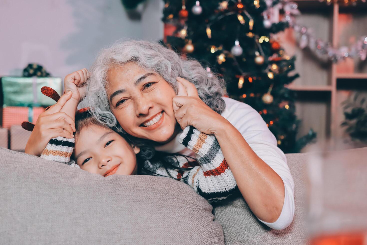 Happy family on Christmas morning. Affectionate grandmother and cheerful granddaughter open a holiday gift together at home photo