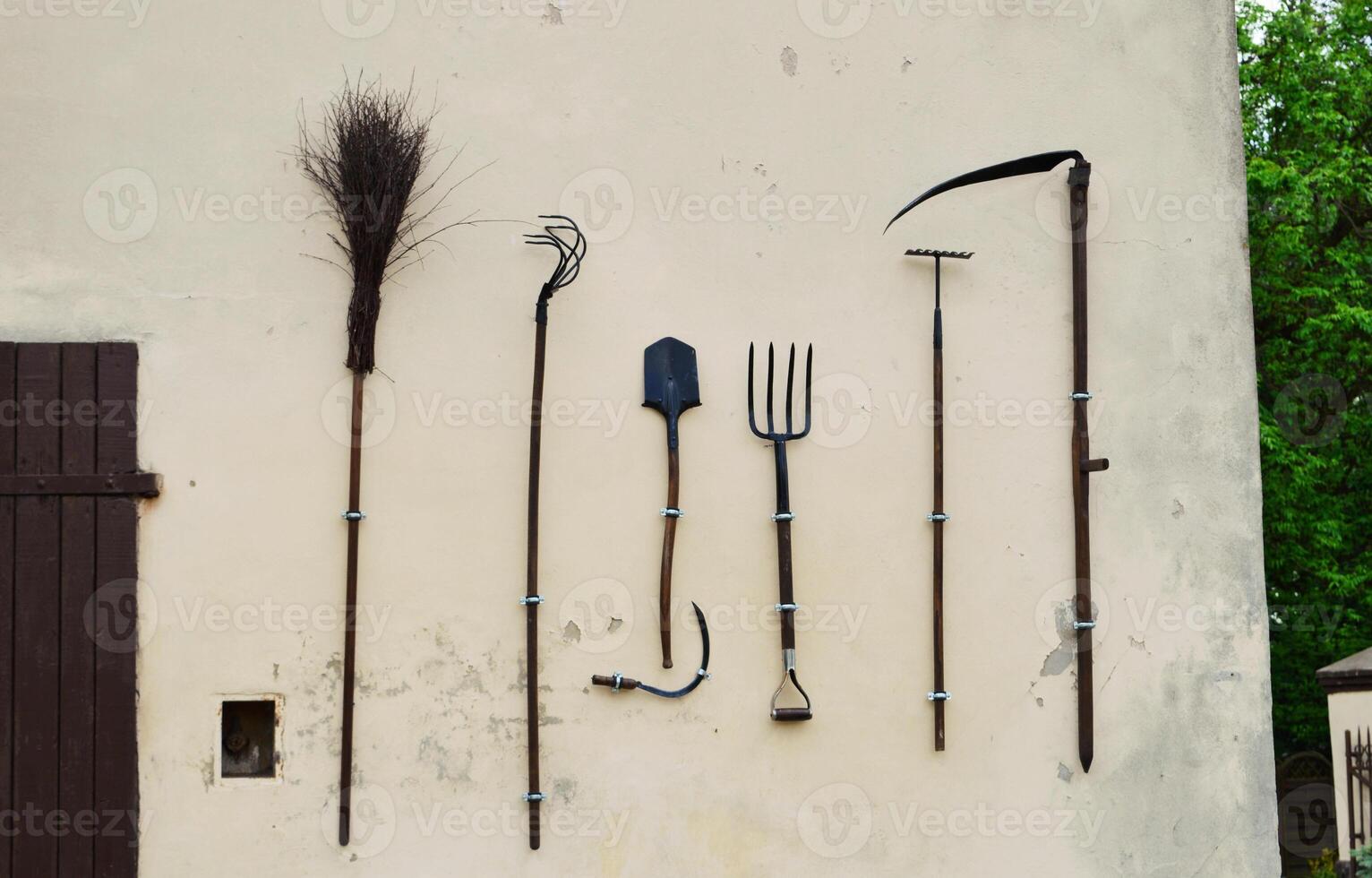 On the wall of the shed hangs a set of gardening tools. photo