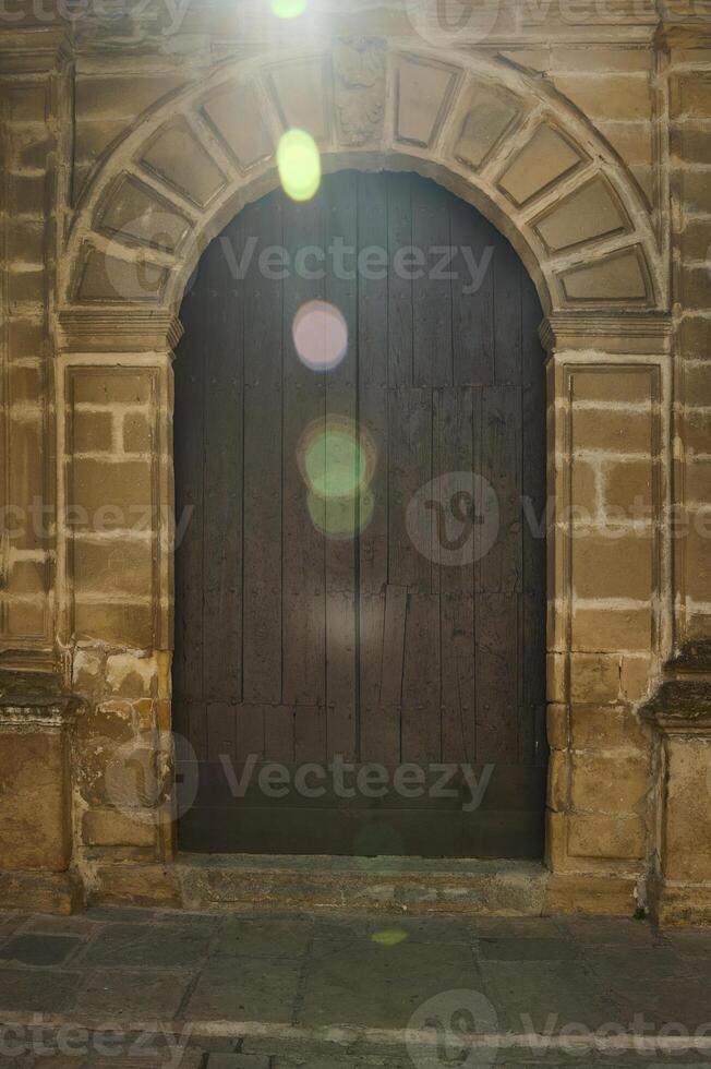 Rustic wooden door with stone archway and sunlight flare photo