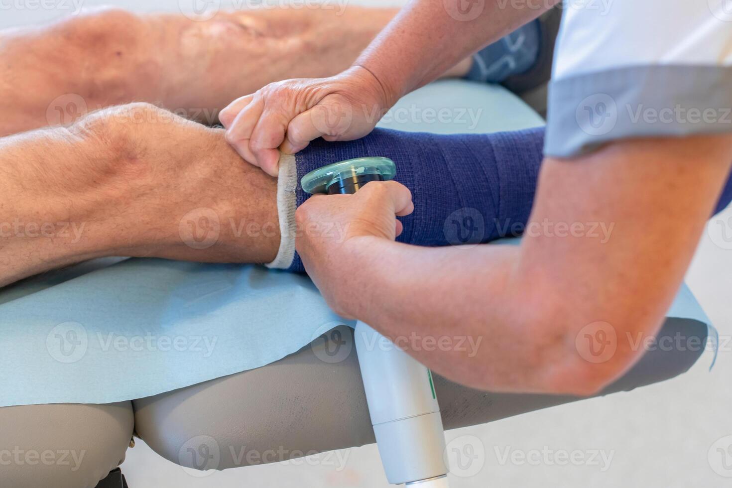 Nurse in clinic carefully cuts strong fiberglass cast on patient's leg with plaster saw according to instructions, taking precautions, patient sits quietly, professional help concept, photo