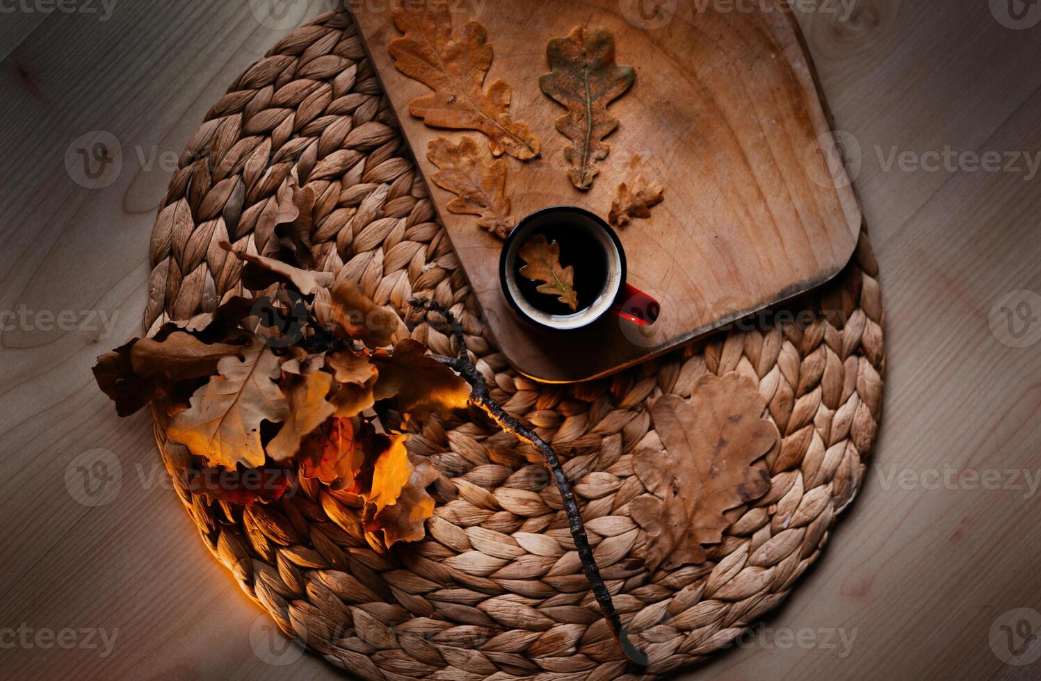 a cup of coffee with an oak leaf stands on a wicker napkin, a twig and a board lie nearby photo
