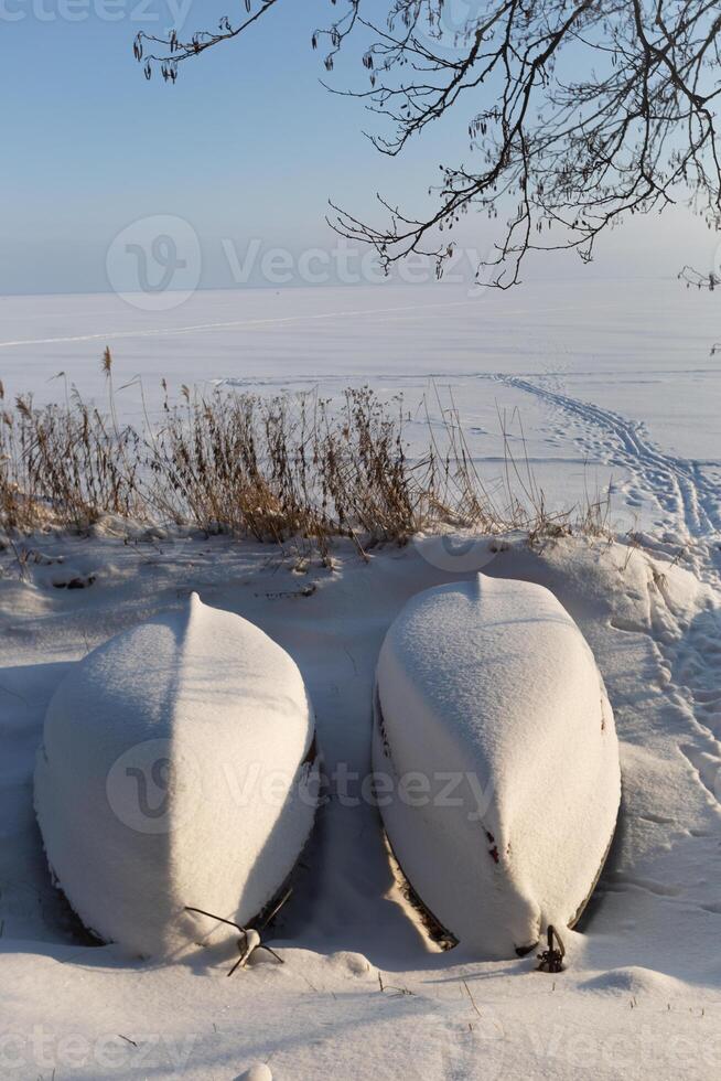 two boats on the shore of a lake in winter are standing under the snow photo