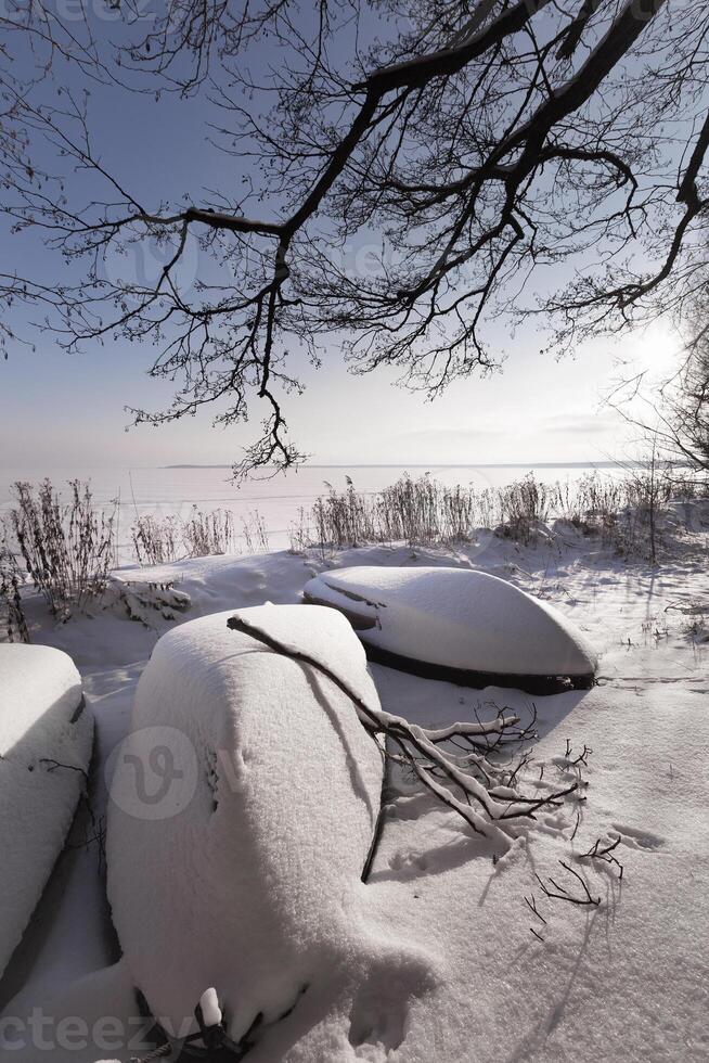 boats on the lake shore in winter stand under the snow photo