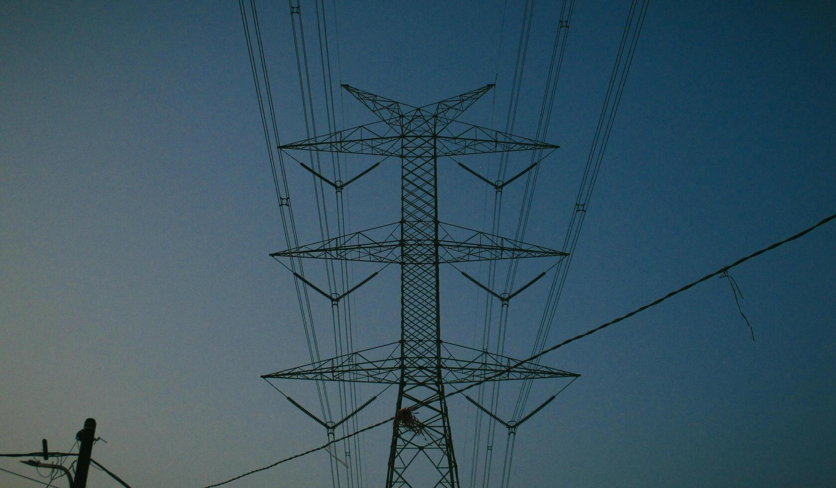 A towering electricity pylon with power lines stretches across the sky at dusk, creating a silhouette against the fading light, symbolizing energy and infrastructure. photo