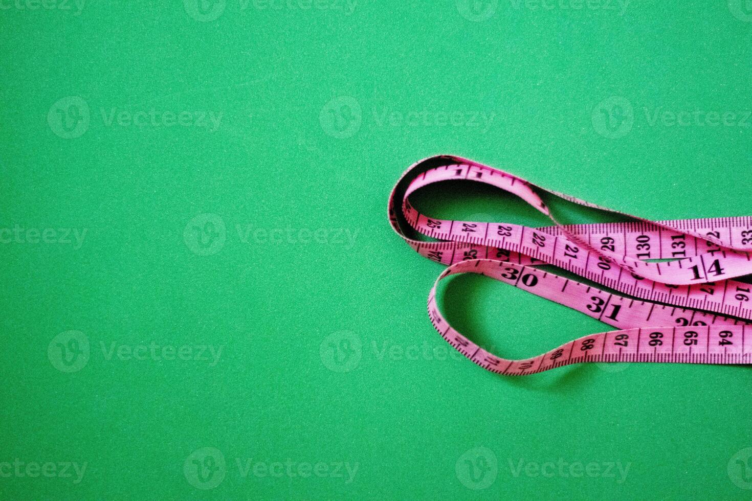 Pink measuring tape on green background photo
