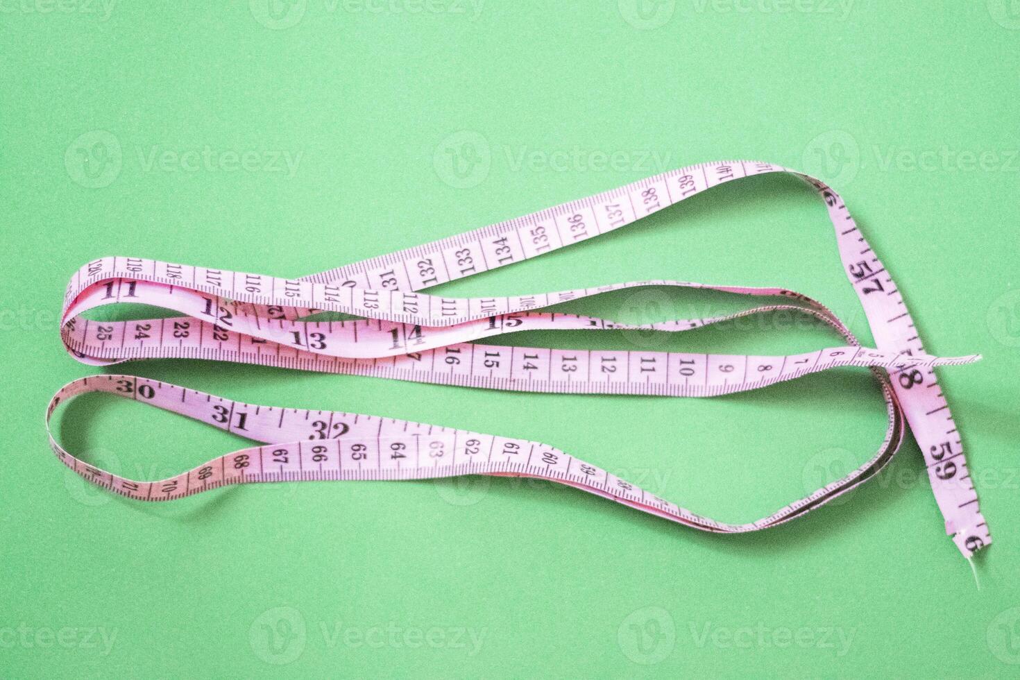 Pink measuring tape on green background photo
