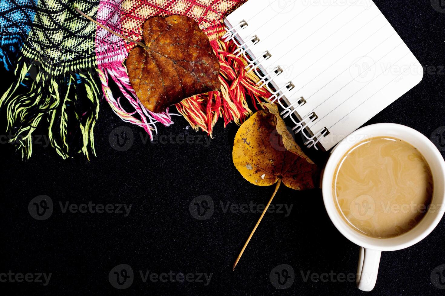 The comfort of being at home in autumn. The photo above is of a cup of hot coffee, a patchwork blanket, maple leaves, on a black isolated background with copy space