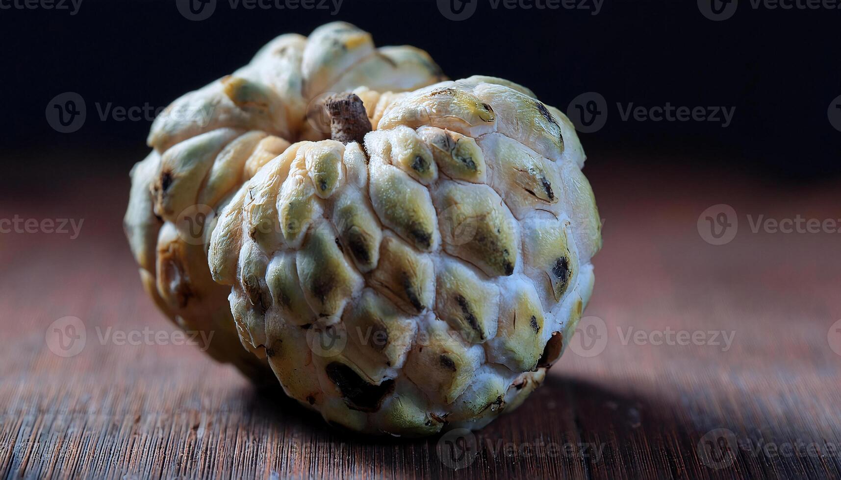 close-up of custard apple with cracked segments and visible mold on wooden surface under moody lighting photo