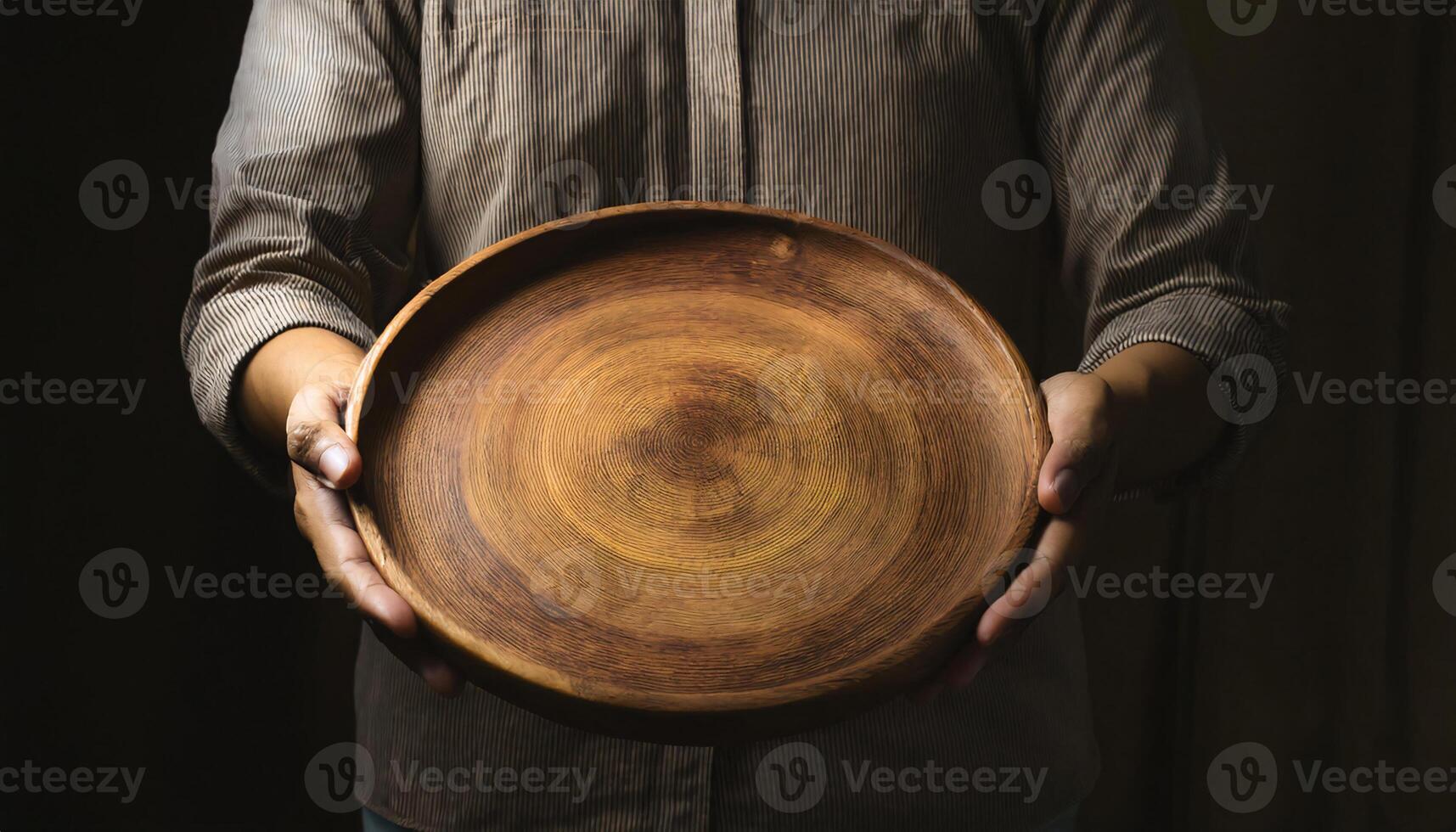 hands holding a handcrafted wooden plate with intricate wood grain patterns against a dark background photo