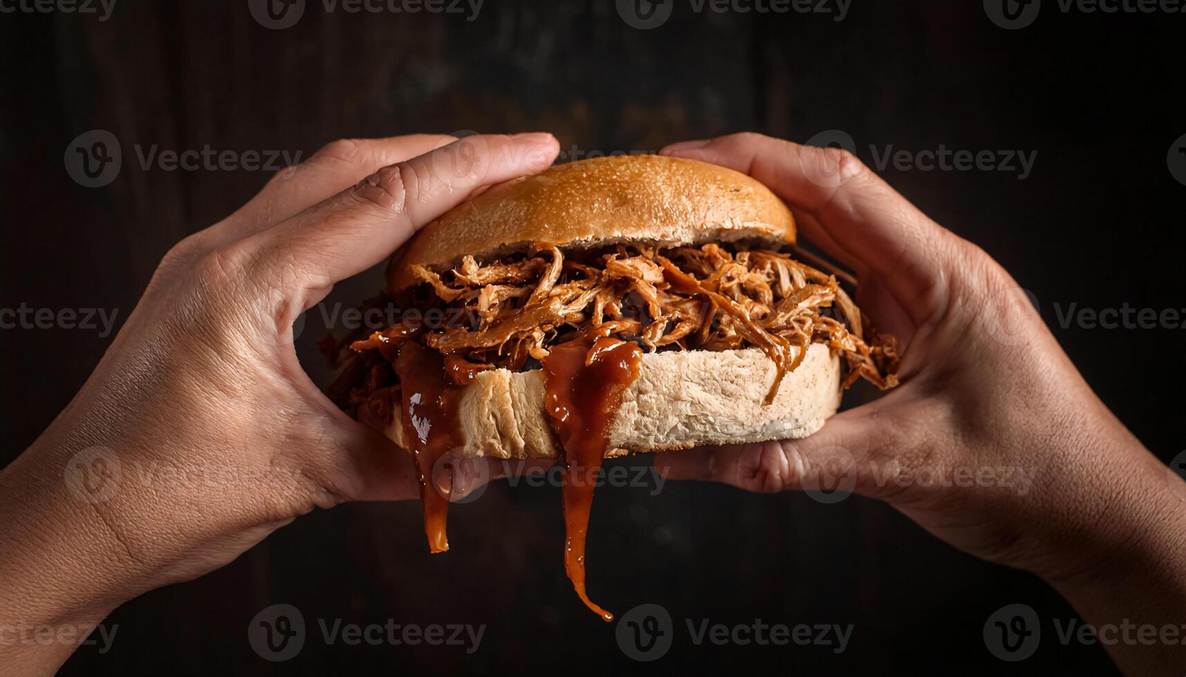 close-up of hands gripping a pulled pork sandwich with barbecue sauce oozing from the sides against a dark rustic background photo