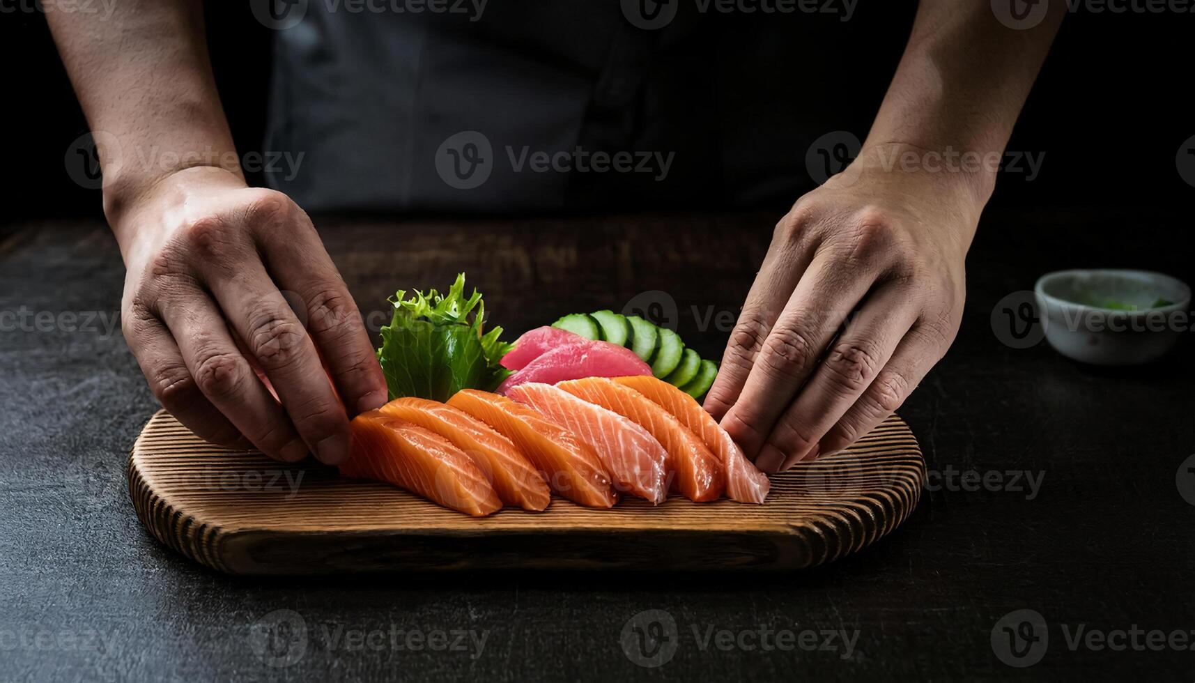 close-up of hands arranging fresh salmon sashimi slices on a wooden platter with garnishes of cucumber, tuna, and greens photo