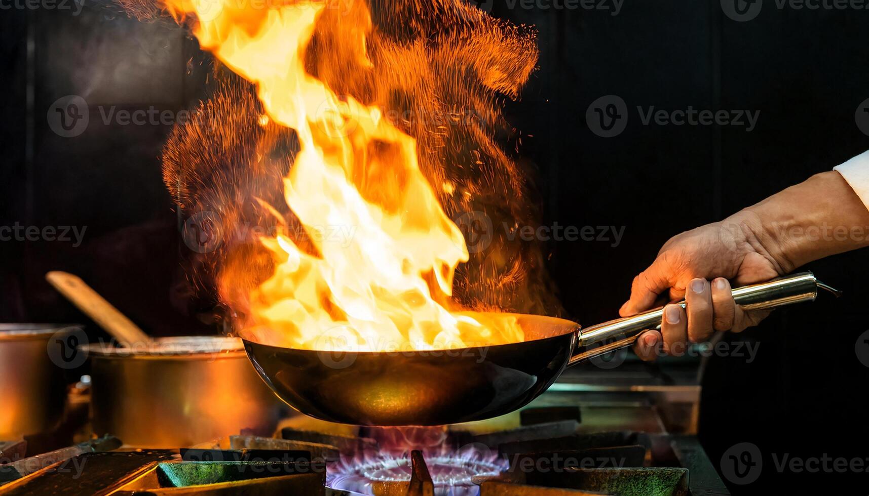 close-up of a chef hands holding a pan with dramatic flames rising in a high-energy professional kitchen scene photo