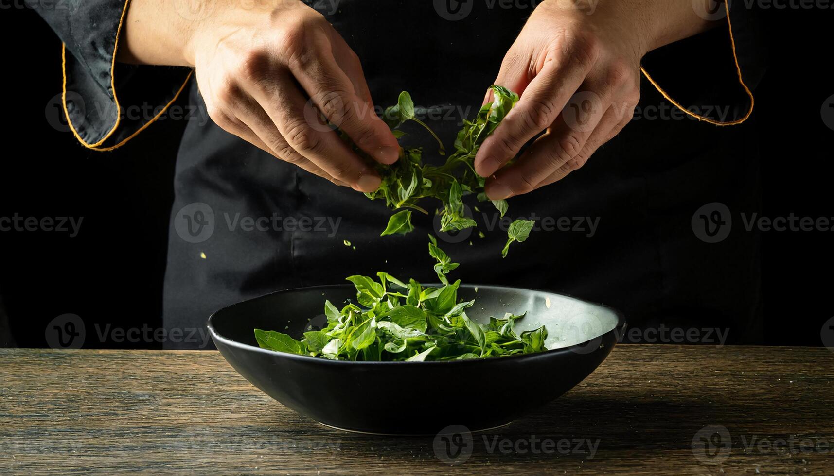 chef hands tossing fresh basil leaves into a black bowl, preparing a vibrant and healthy herb salad photo