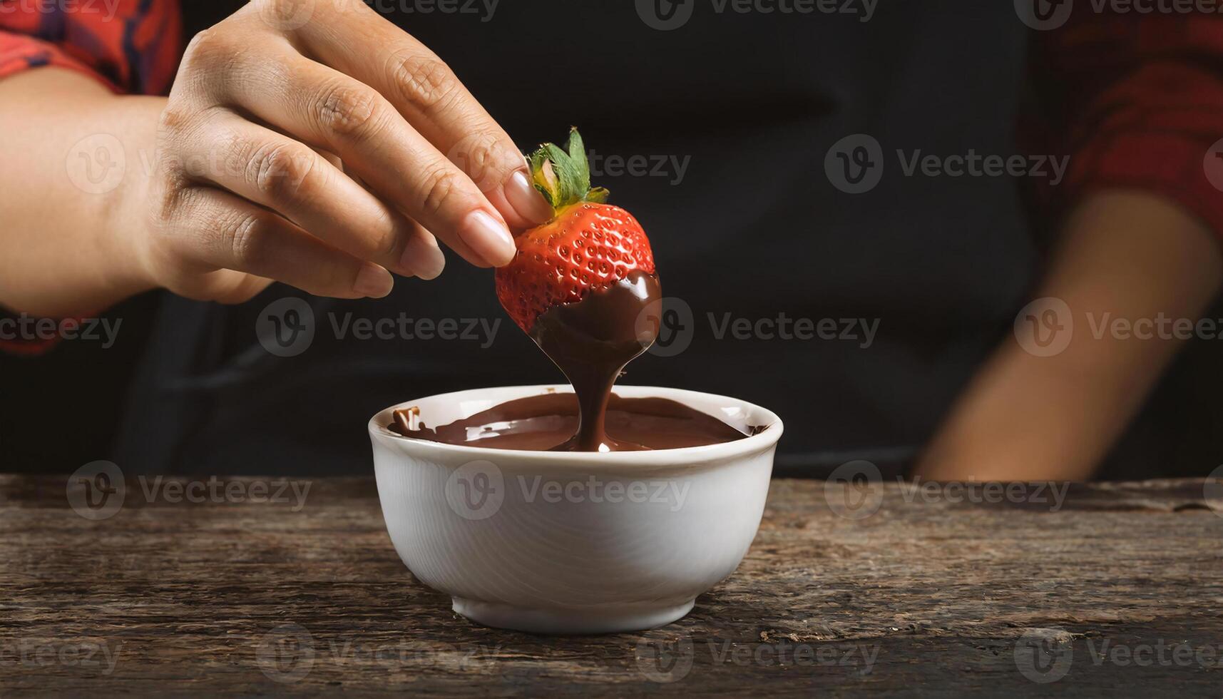 close-up of hands dipping fresh strawberries into melted chocolate, creating a rich dessert treat on a wooden table photo
