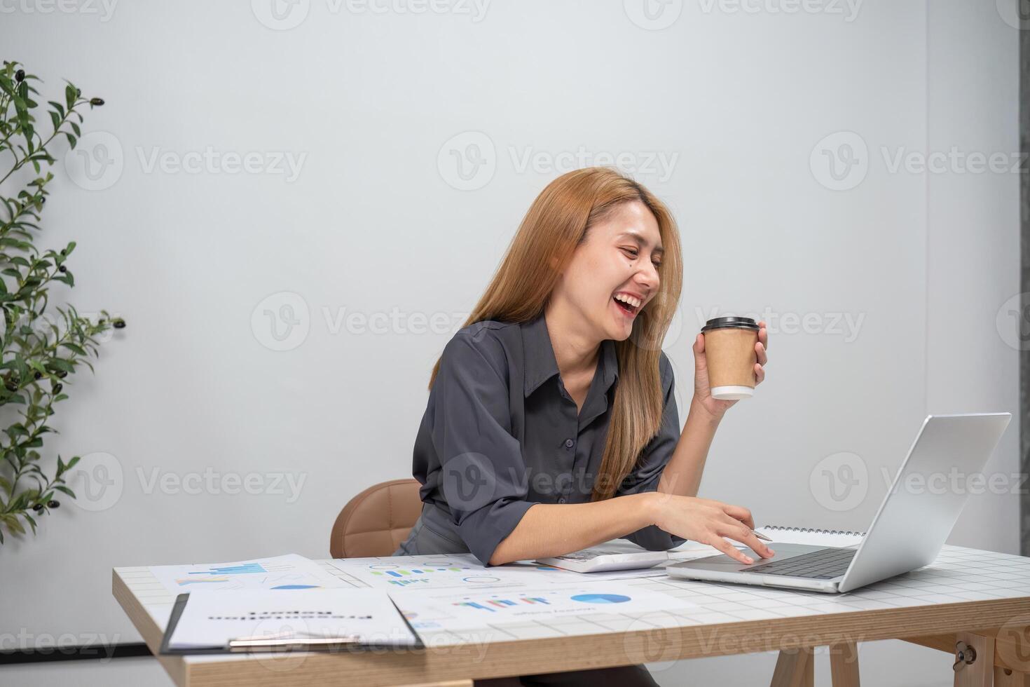 Young Female Accountant Working on Financial Accounting Tasks with Laptop and Coffee in Modern Office Setting photo
