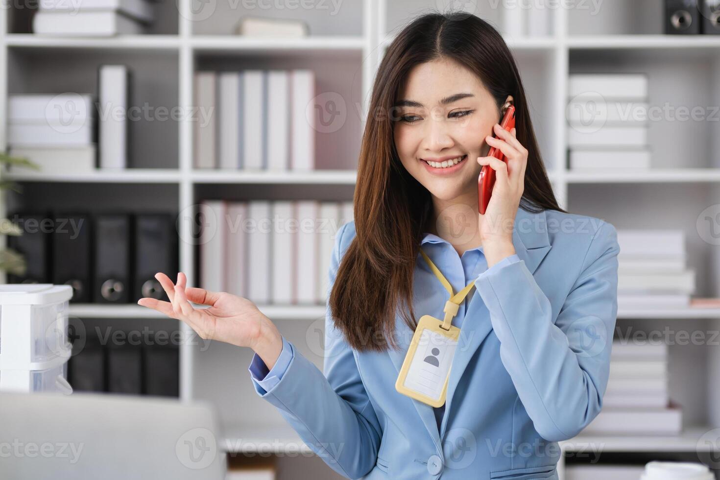 Young Female Accountant in Modern Office Environment, Smiling and Talking on Phone, Professional Businesswoman at Work, Confident and Focused, Office Background with Shelves and Documents photo