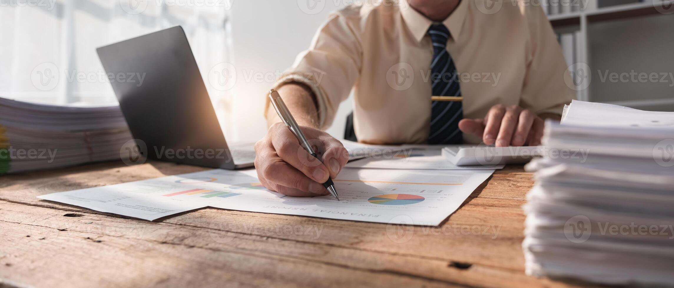 Businessman Working in Modern Office with Documents and Laptop on Wooden Desk, Analyzing Financial Data and Reports, Professional Corporate Environment, Sunlight Streaming Through Window photo