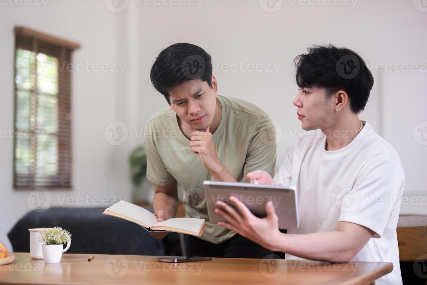 Young Gay Couple Sitting Together at Home, Engaging in a Discussion with a Book and Tablet photo
