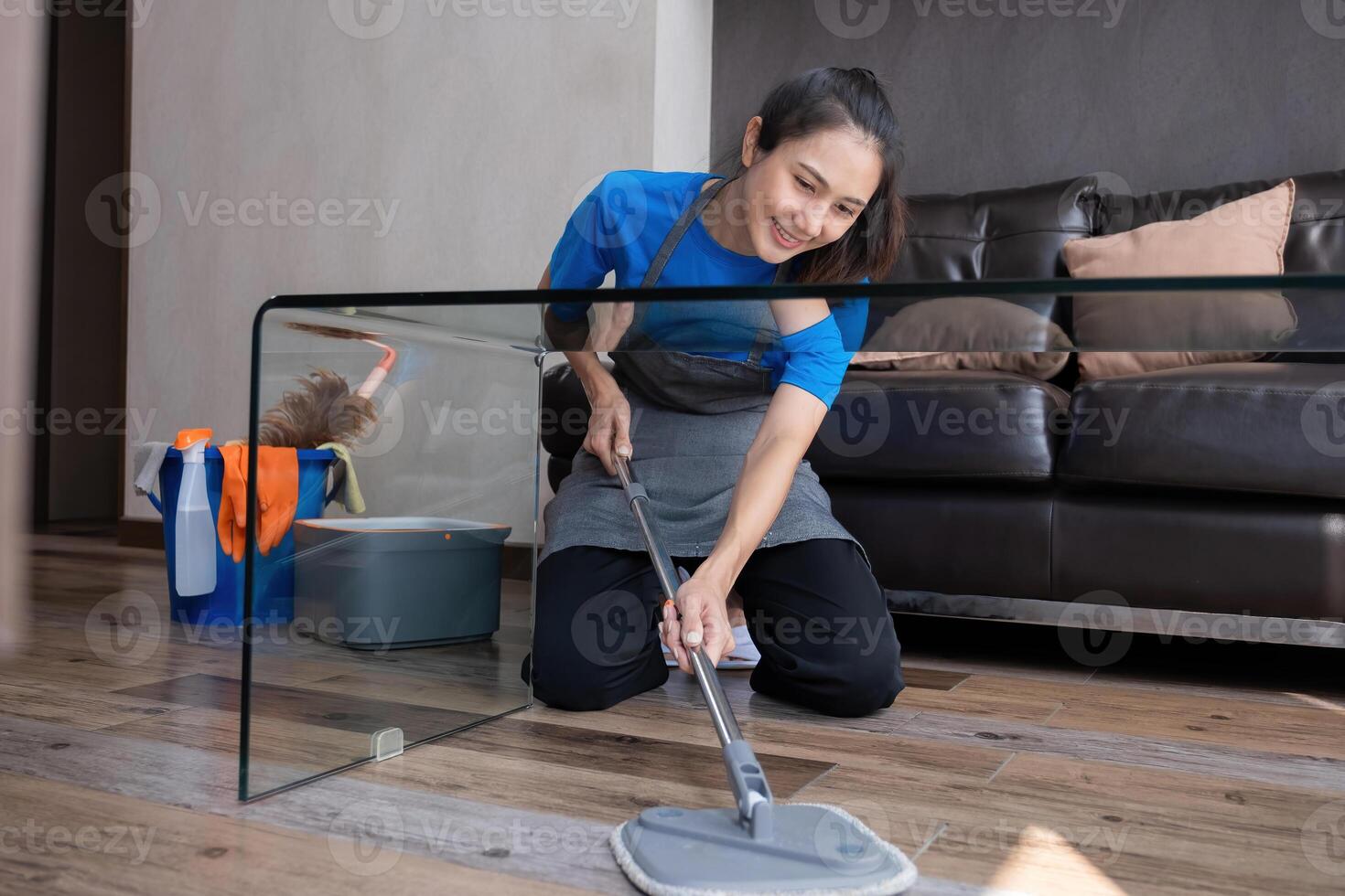 Smiling housekeeper mopping floor in living room with cleaning supplies. Concept of domestic chores and hygiene photo