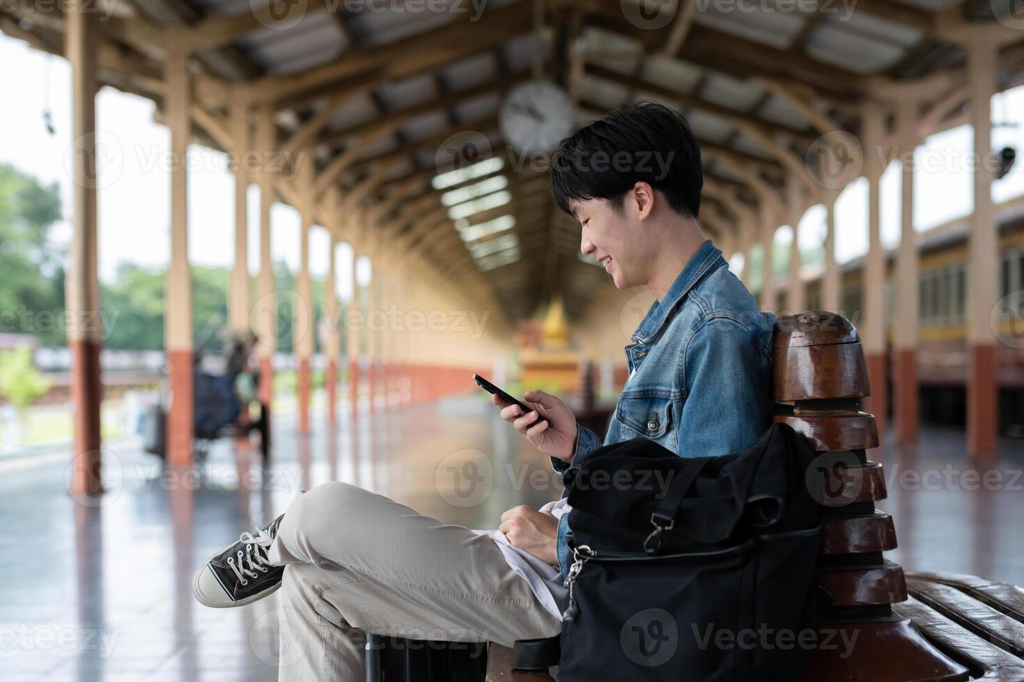 Young man with backpack checking social media on phone waiting for train at train station to travel photo