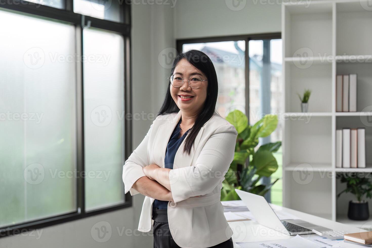 Confident Business Woman Standing in Modern Office with Arms Crossed, Smiling and Looking at Camera photo