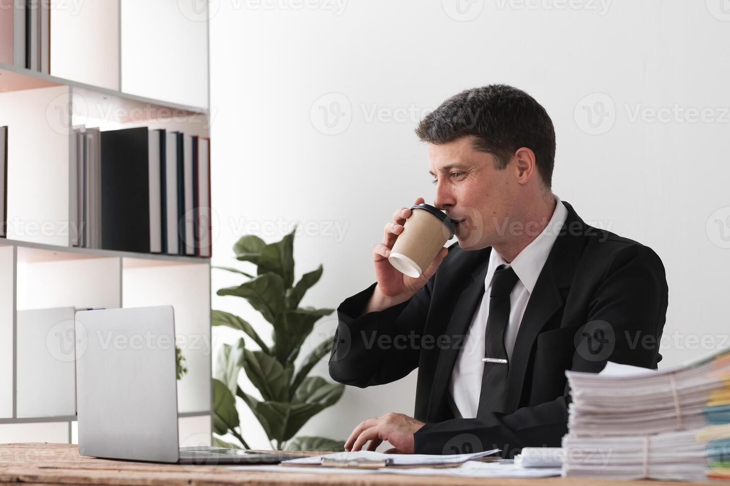 Businessman drinking coffee while working at desk with laptop, concept of break and focus photo