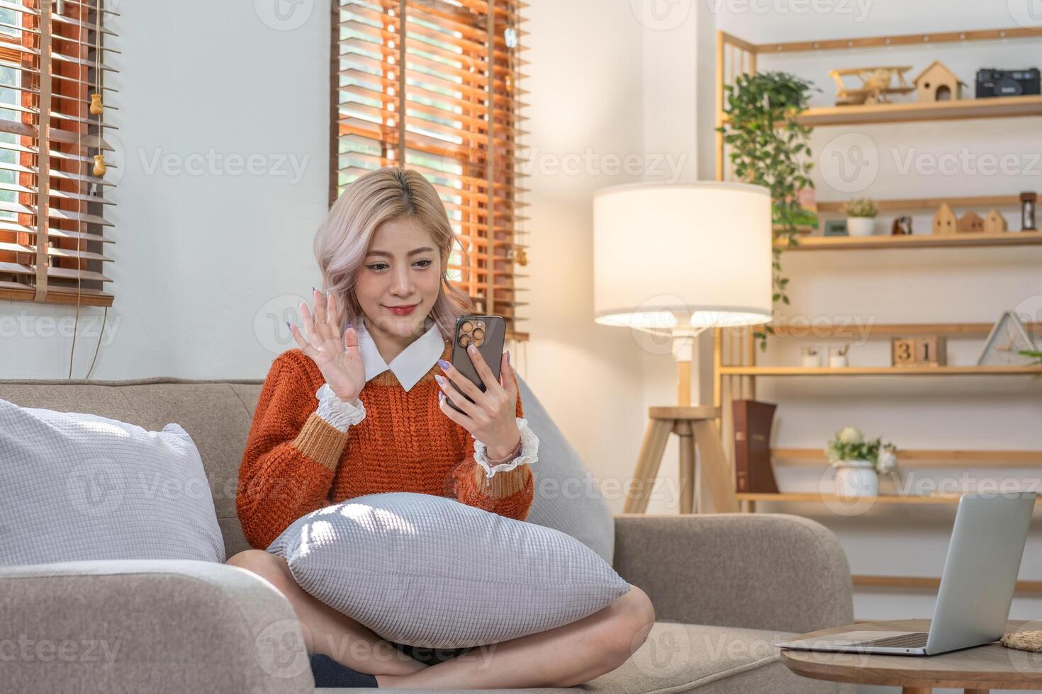 Beautiful young woman sitting on the phone, chatting with friends via call, resting and relaxing in the living room. photo