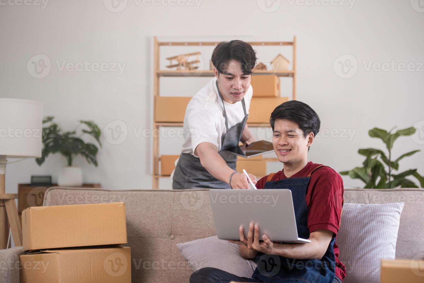 A gay couple running a small business takes order on a laptop and sells product online together in a room full of boxes. photo