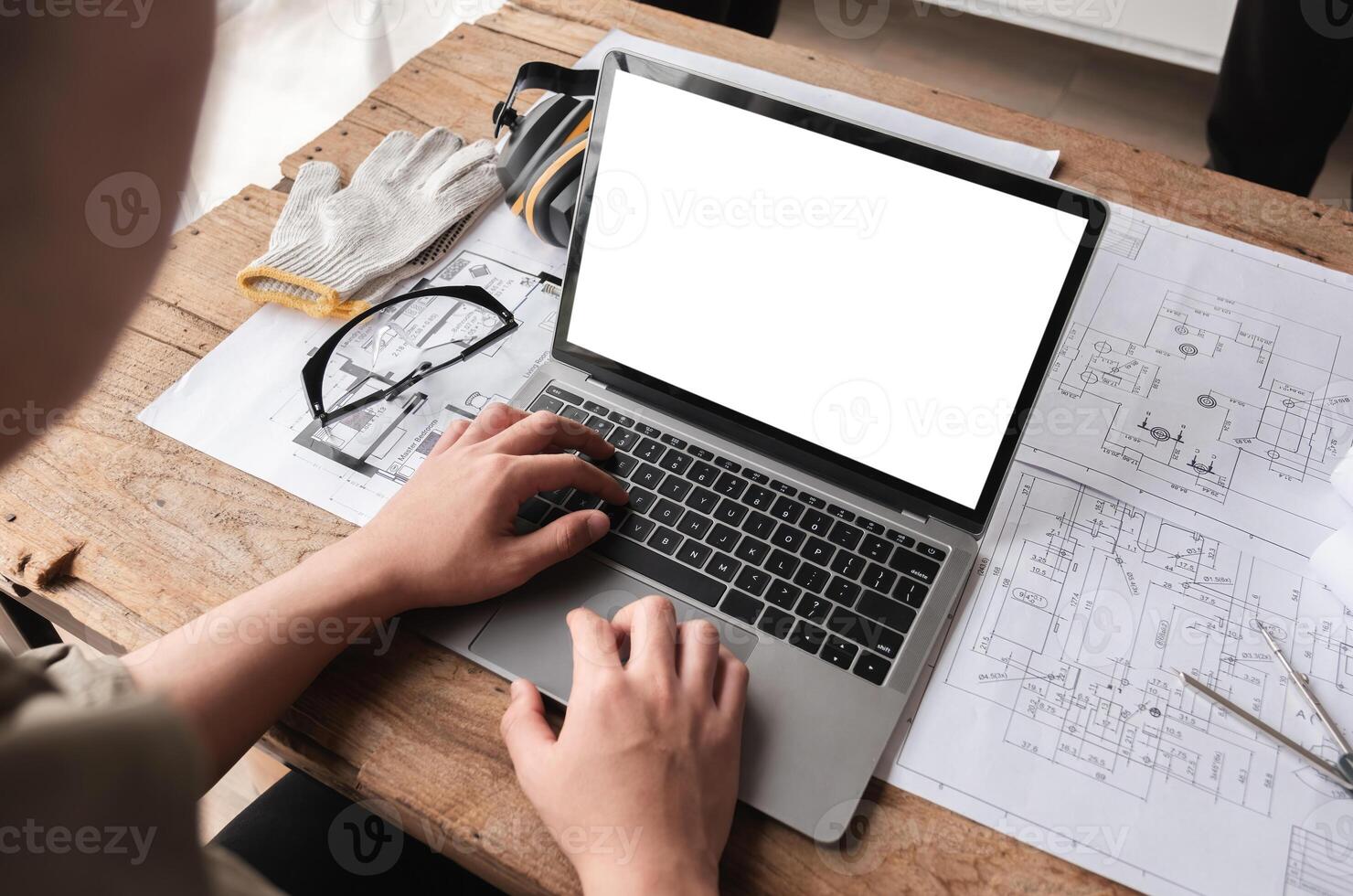 Engineering Team Collaborating on Work Plans with Laptop with white screen and Blueprints on Wooden Table photo