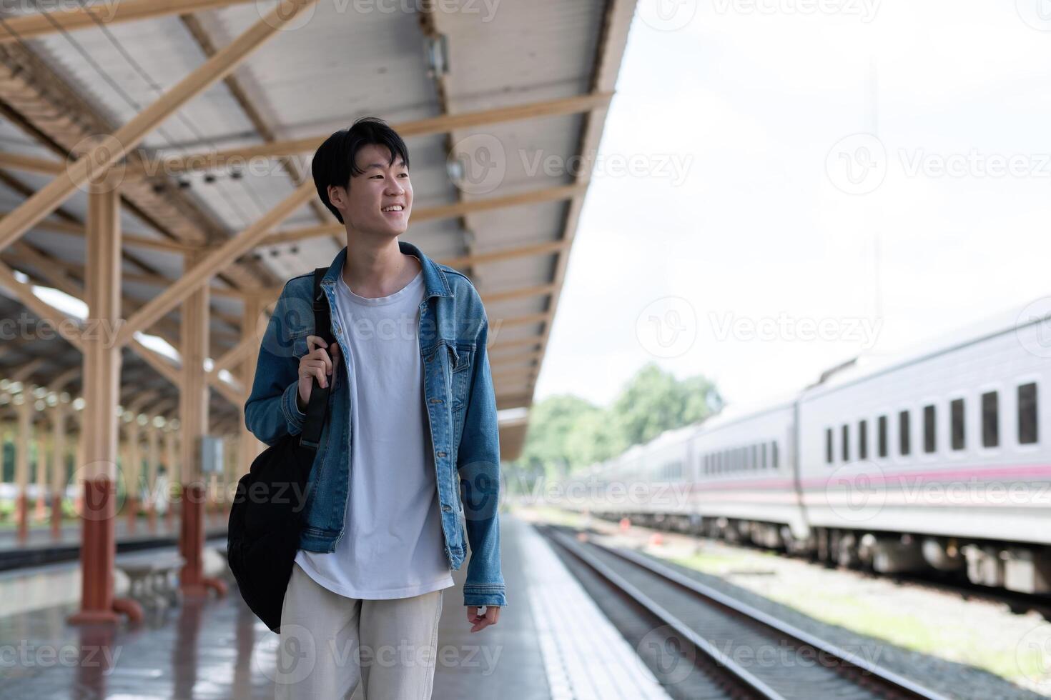 A young man carries a backpack and waits for the train at the train station to travel. photo