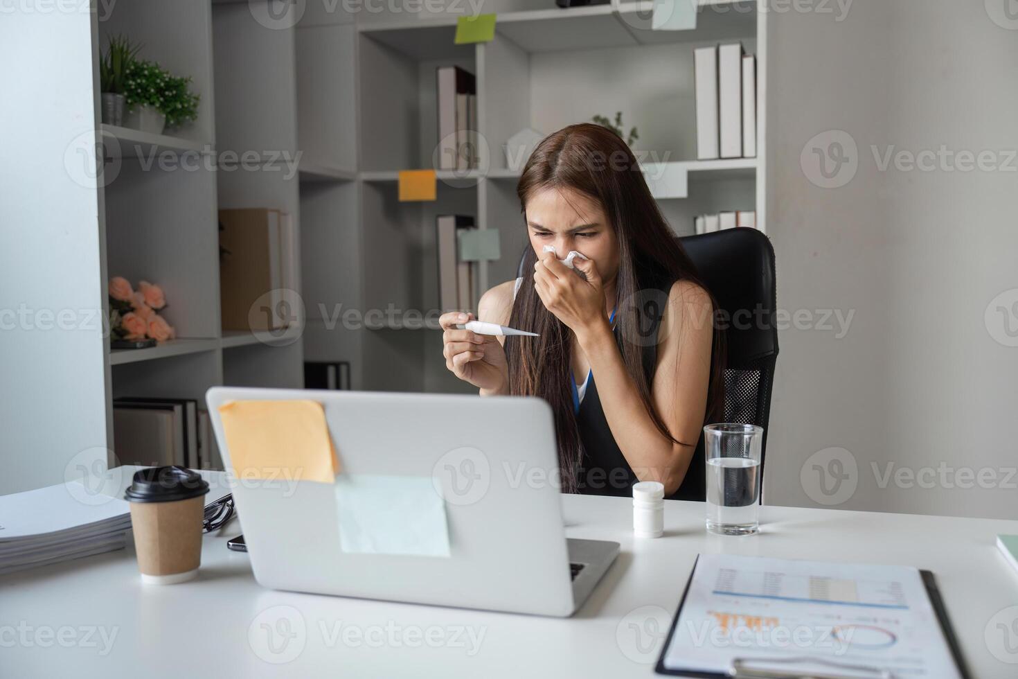 Young Female Office Worker with Cold Sneezing at Desk in Modern Workplace Setting with Laptop and Coffee photo
