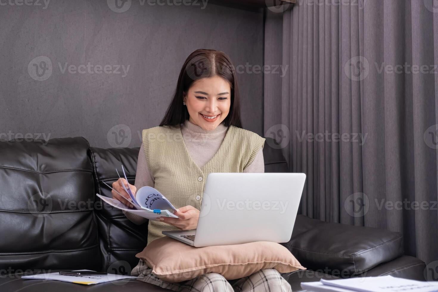 Woman Using Laptop and Reading Document on Sofa. Concept of multitasking and modern work lifestyle. photo