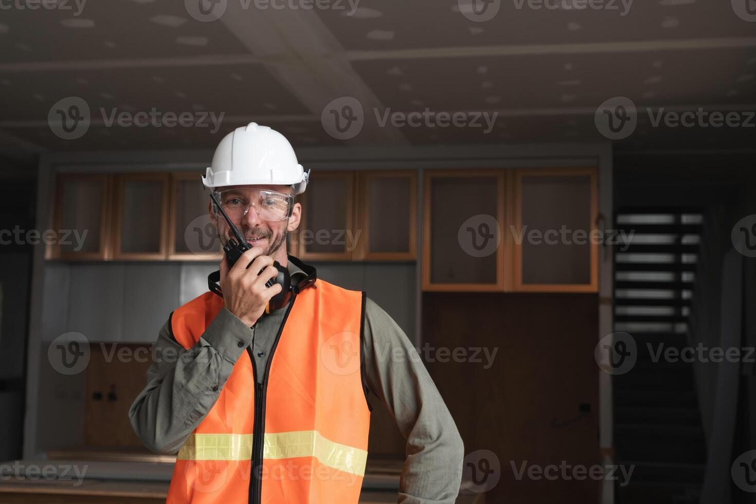 Young Engineer at Construction Site Wearing Safety Gear and Communicating via Radio in Modern Building Under Construction photo