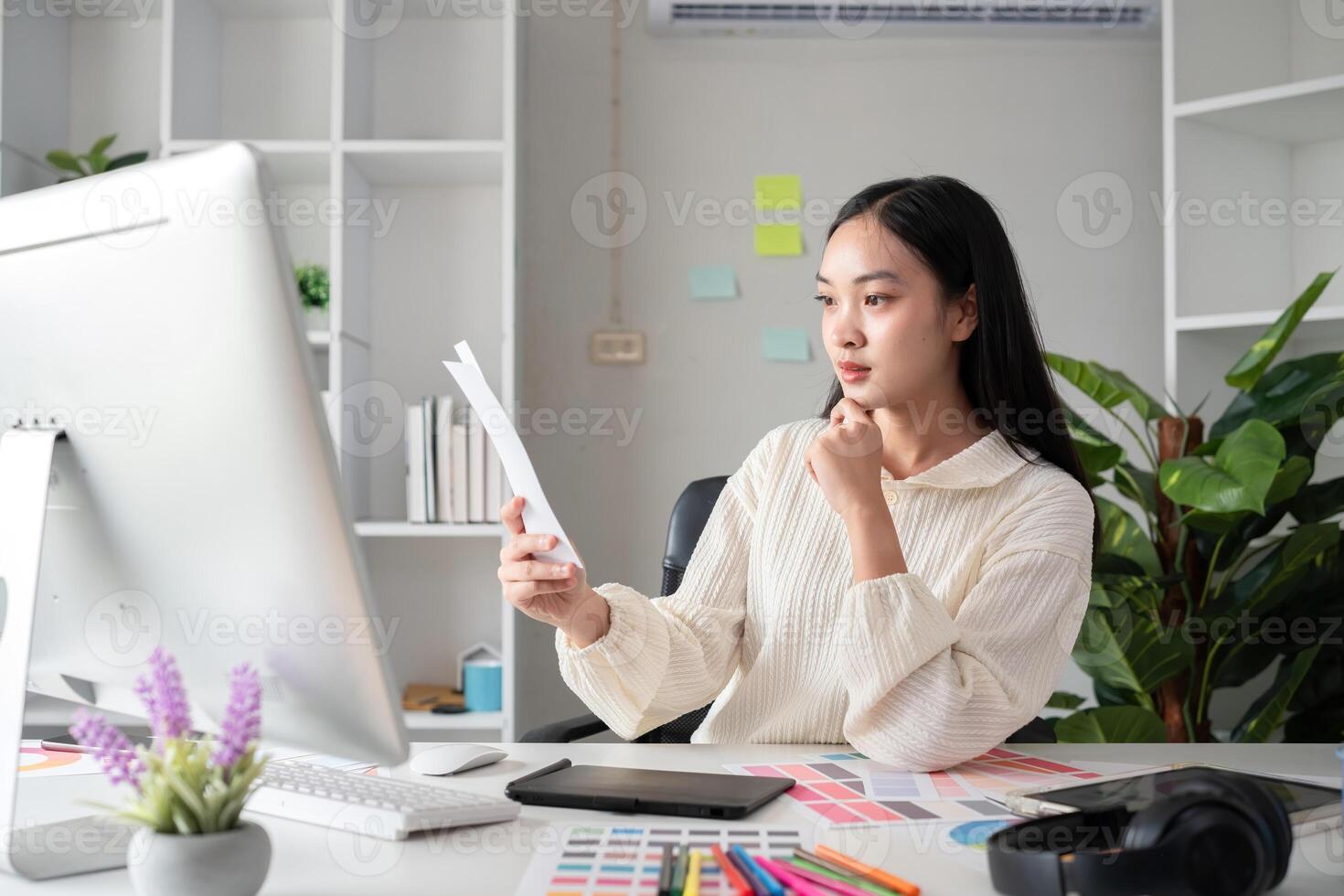 Female designer working in graphic design Choose colors for graphic design work. Focused work on a table full of colored paper for working on a computer photo